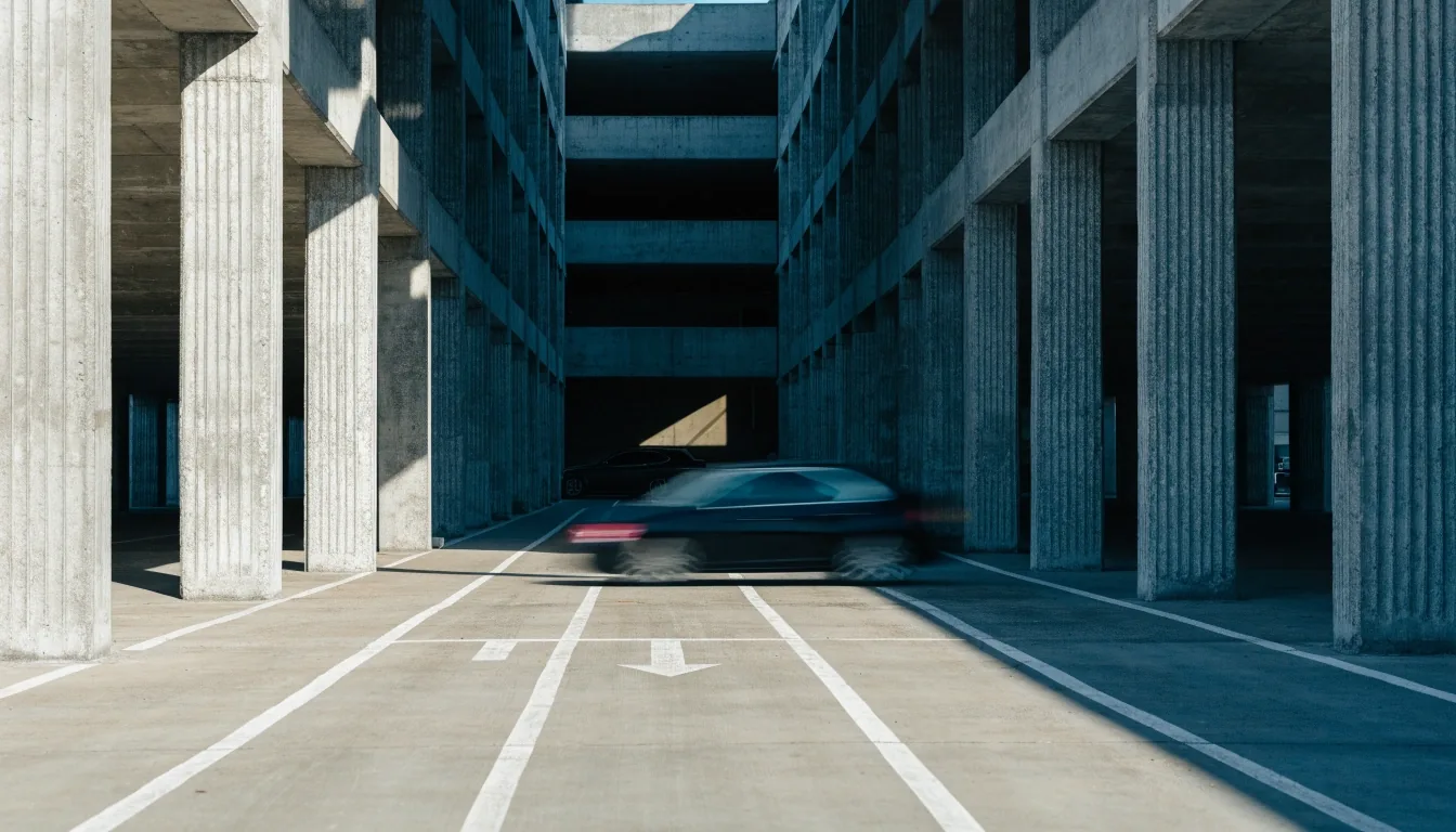 Concrete multi-storey parking deck in cold morning light with painted lane markings and a car crossing the frame